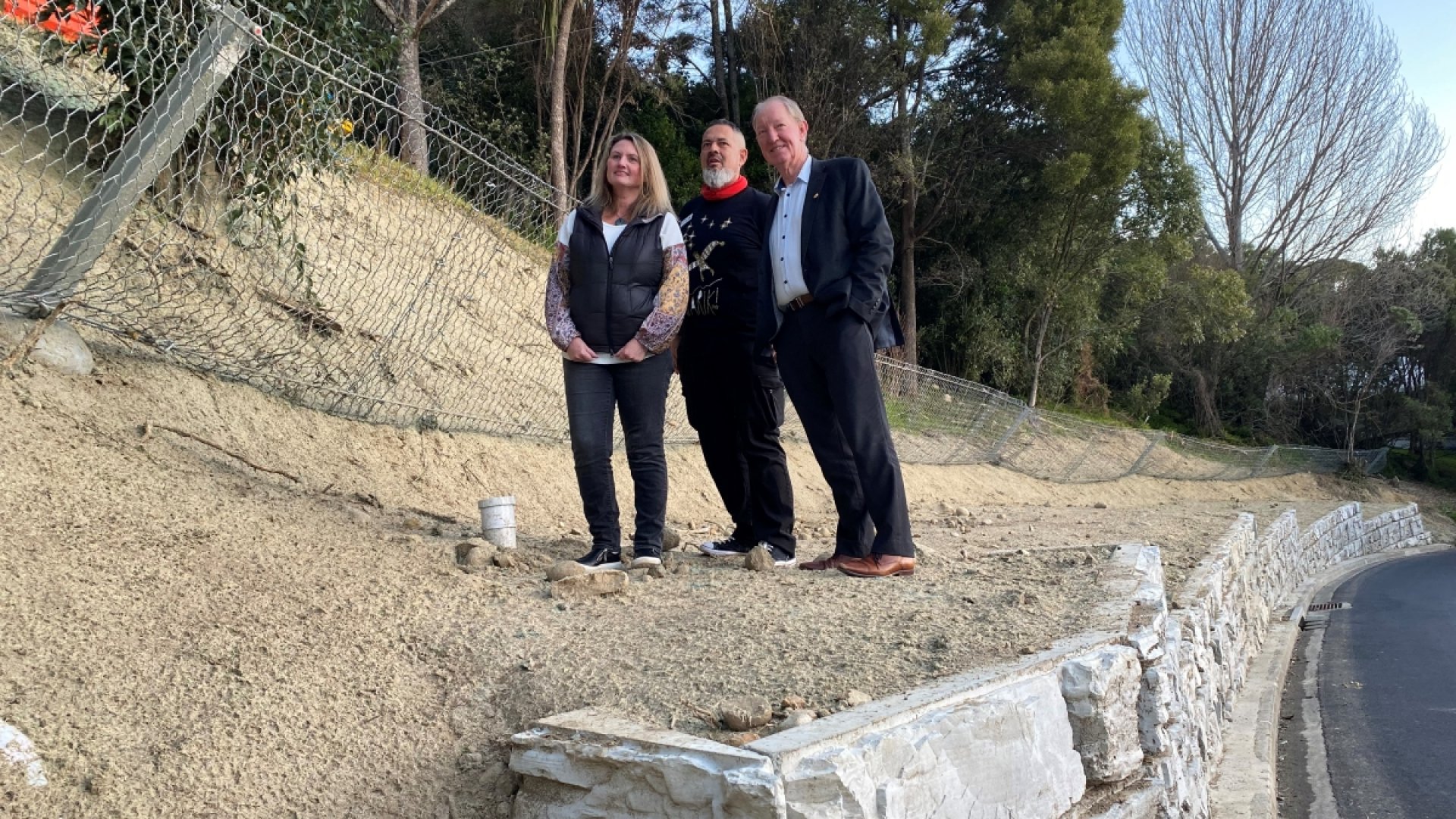 Members of the Nelson City Council Storm Recovery Taskforce Councillor Trudie Brand, Councillor Matty Anderson and Mayor Nick Smith inspect the rockfall protection fence and block retaining wall along Moana Avenue.