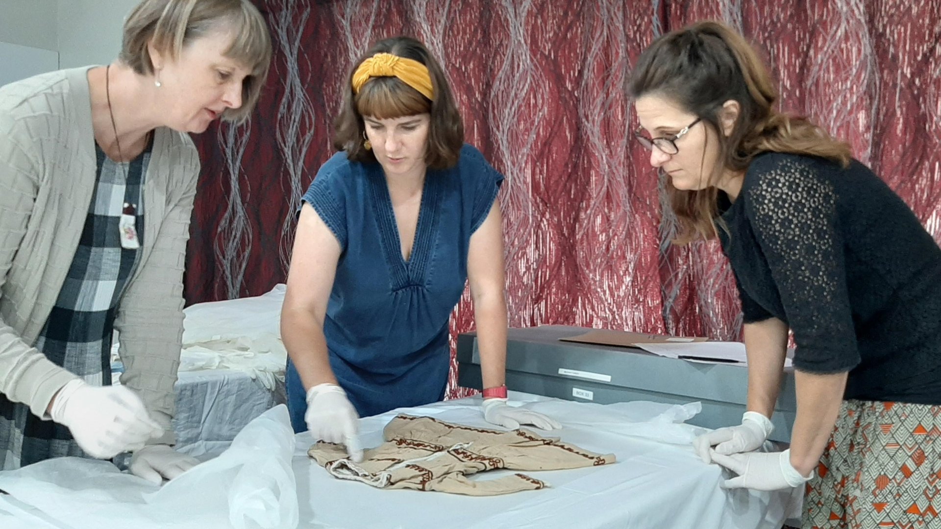 Dr Stella Lange, left, inspects a Victorian-era child’s dress with Jessie Bray Sharpin and Mahina Marshall before it is repacked and stored.