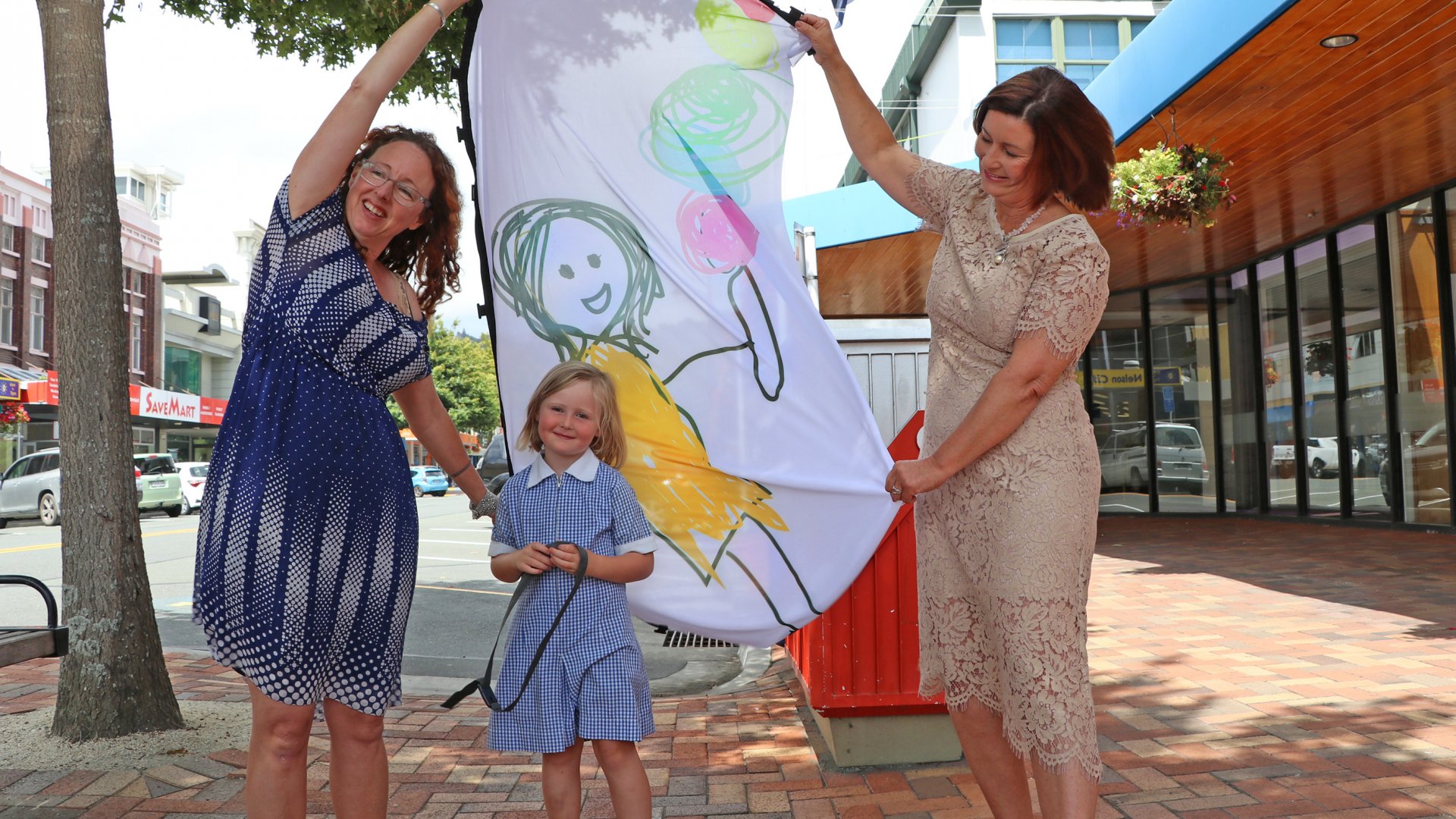 Rebekah Malthus, left, with daughter Jeanie Hicks, 5, and Mayor Rachel Reese check out the flag bearing Jeanie's artwork before it was raised outside Civic House on Tuesday.  